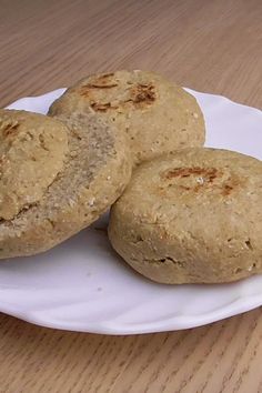 three biscuits on a white plate sitting on a wooden table