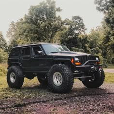 a black jeep parked on top of a dirt road next to some grass and trees