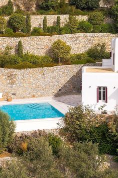 an aerial view of a house with a pool in the foreground and stone walls surrounding it