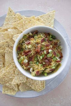 a white bowl filled with food next to tortilla chips on top of a plate