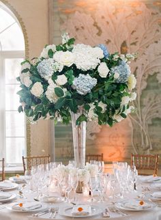 a tall vase filled with white and blue flowers on top of a table