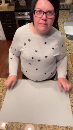 a woman standing in front of a piece of paper on top of a counter next to candles