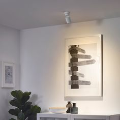 a living room with white furniture and art on the wall above it, along with a potted plant