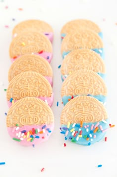 several cookies with sprinkles and colored frosting are lined up on a white surface