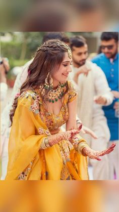 a woman in yellow and gold dress holding her hands out to the side with other people behind her