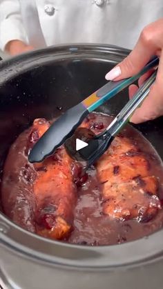 a person is using tongs to stir food in a pot with sauce and meat