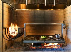 an outdoor grill with flames and food cooking on the grill, in front of a brick wall