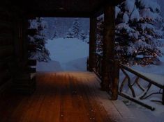 a porch covered in snow next to a forest filled with lots of trees and lights