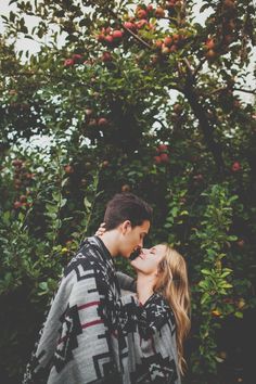 a man and woman standing next to each other in front of fruit trees