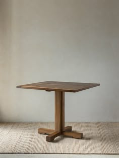 a square wooden table sitting on top of a carpeted floor next to a wall