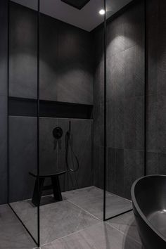 a black bathtub sitting next to a shower in a bathroom with dark walls and flooring