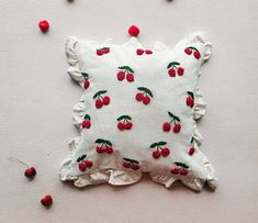 a white pillow with red cherries on it and scattered cherries around the cushion