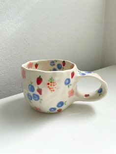 a white cup with blue and red berries on it sitting on top of a table