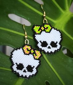 the skull earrings are decorated with beading and beads, which have been placed on top of a green leaf