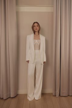 a woman standing in front of curtains wearing a white suit