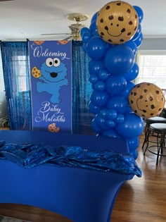 a blue table topped with balloons next to a large cookie monster sign and balloon decorations