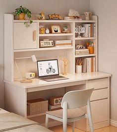 a white desk with a laptop computer on top of it next to a chair and bookshelf