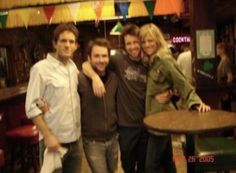 three men and a woman posing for a photo in a bar with flags hanging from the ceiling