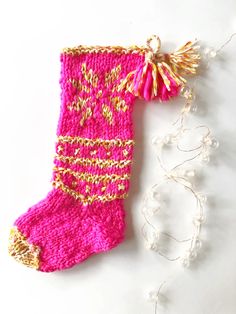 a knitted stocking hanging from a string on a white surface with beads and thread