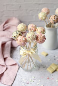 some cake pops are in a glass vase on a table with confetti and marshmallows