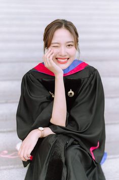 a woman sitting on the ground wearing a graduation gown and holding her hand to her face