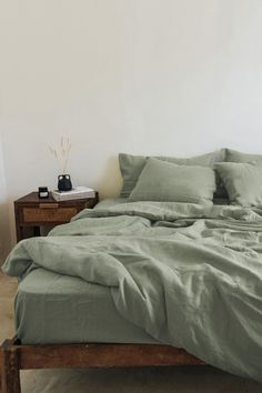 a bed with green sheets and pillows in a room next to a night stand on the floor