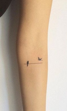 a small tattoo on the arm of a woman with two birds flying above her head