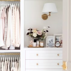 an open closet with clothes hanging on the wall and flowers in vase next to it