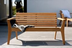 a wooden bench sitting on top of a patio next to two chairs and a blanket