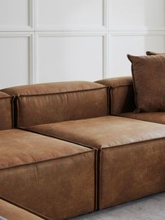 a brown leather couch with two pillows on it's back and one arm facing the camera