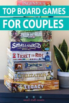 a stack of board games sitting on top of a table next to a potted plant