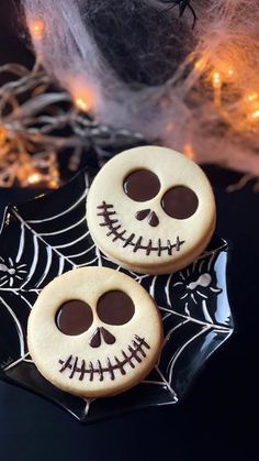 two decorated sugar cookies on a plate with spider webs and lights in the background