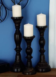 three candles sitting on top of a wooden table next to a blue wall with a clock