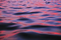 the water is pink and blue with some ripples on it's surface at sunset