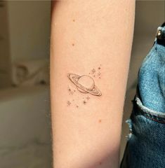 a small saturn tattoo on the right inner arm, with stars in the sky above it