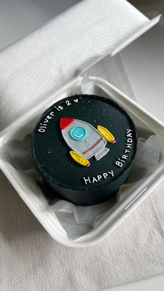 a birthday cupcake with a rocket ship on it in a white box and some napkins