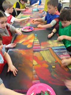 children are sitting at a table painting on paper plates