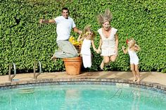 a family jumping into a swimming pool in front of a green hedge and shrubbery