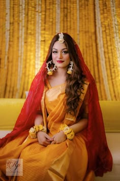 a woman sitting on top of a bed wearing a yellow dress and red shawl