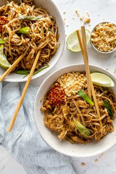 two bowls filled with noodles and vegetables on top of a white tablecloth next to chopsticks