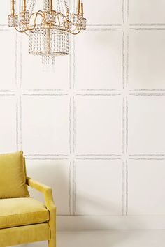 a yellow chair sitting in front of a wall with a chandelier hanging from it