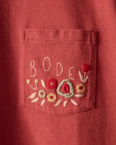 a red shirt with embroidered letters and flowers on the chest pocket that says bode