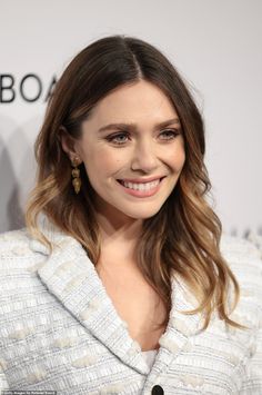 a woman with long hair smiling and wearing a white jacket on top of a red carpet