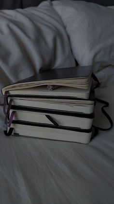 three books sitting on top of each other in front of a white bed sheet and pillows