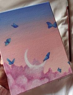 a painting with blue butterflies on it and a pink sky in the background, while someone's hand is holding a paintbrush