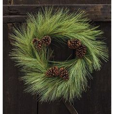 a green wreath with pine cones hanging on a door