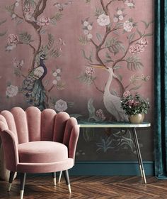 a pink chair sitting in front of a wall with flowers and peacocks on it