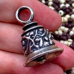 a hand holding a silver bell with beads in the background