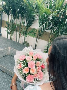 a woman holding a bouquet of flowers in front of some palm trees on the sidewalk