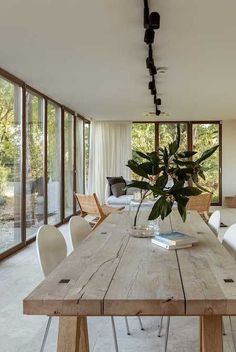 a wooden table with white chairs around it in front of large glass doors and windows